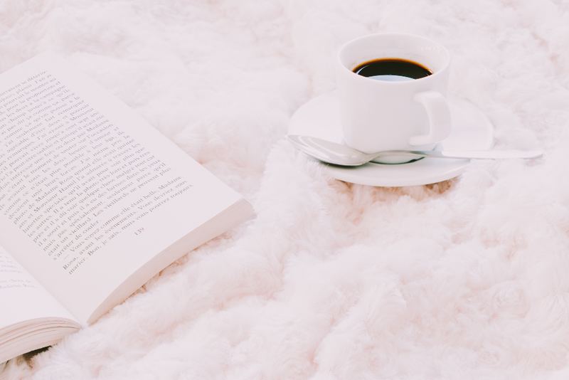 A cup of coffee and an open book on a soft white blanket