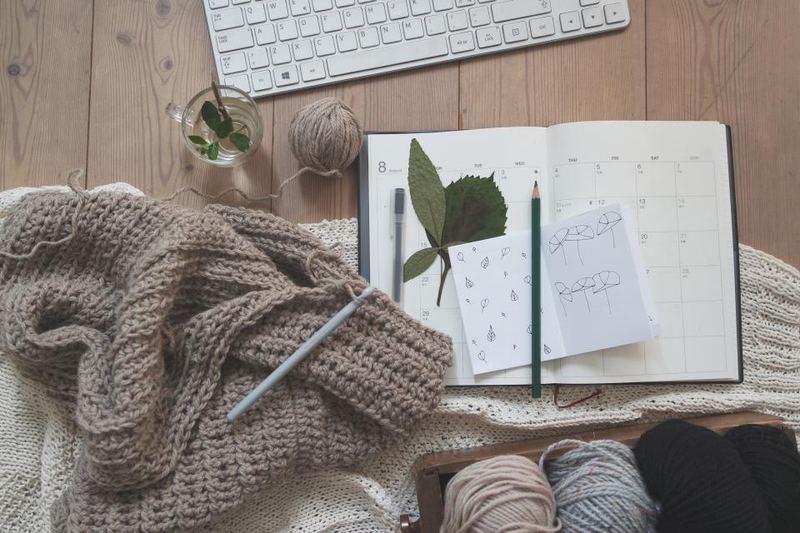 Knitting, yarn and a notebook with sketches on a wooden table